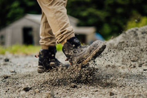 Person walking on a dirt path wearing black Oryx boots and beige pants.